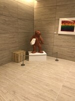 A bear statue on a pedestal in a tiled room with a wooden cabinet and a framed picture on the wall.