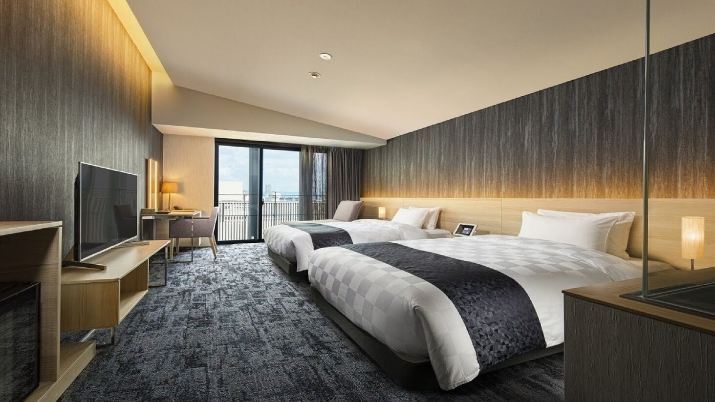 A hotel room with two beds, a TV, a desk, and a balcony with a view.