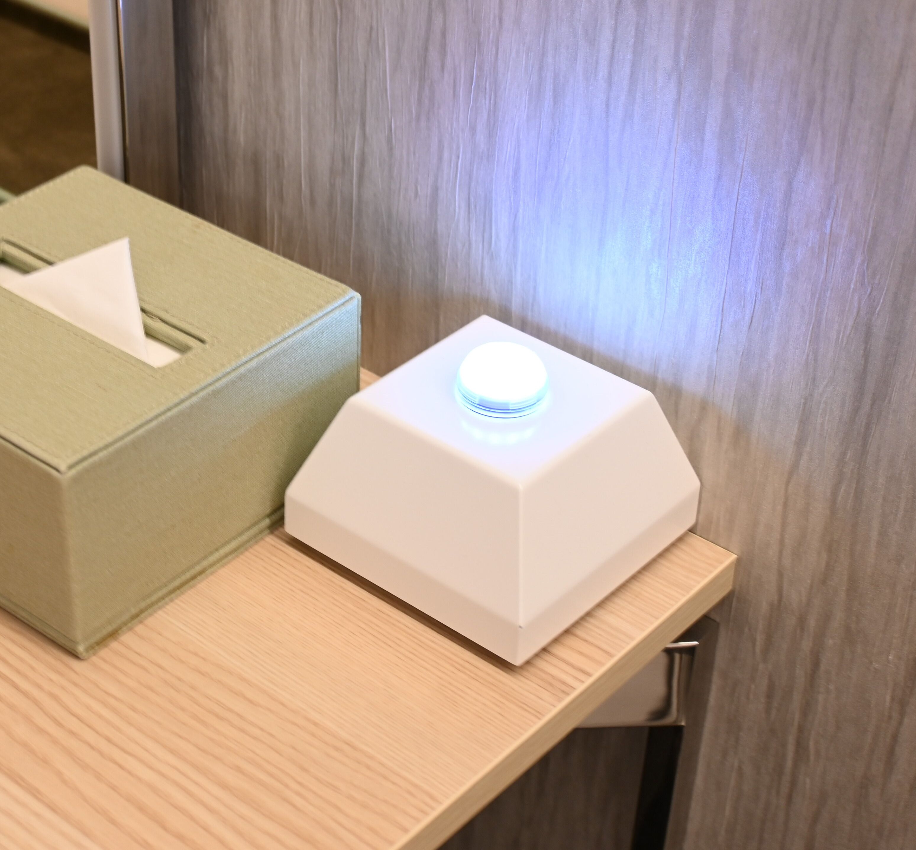 A tissue box and a white device with a blue light on a wooden surface.