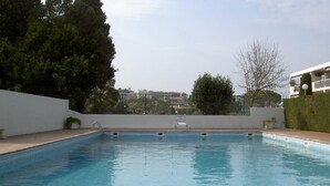 Una piscina rectangular amb un voreig emblat, envoltada per una paret blanca baixa i una tanca.