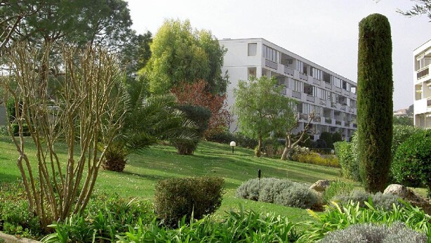 Un edifici modern amb teulada plana i múltiples balcons, envoltat d'una jardineria cuidada i arbres.