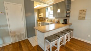 A kitchen with a central island, bar stools, and a microwave.