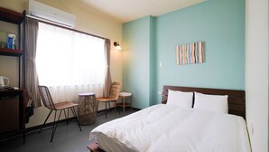 A hotel room with a bed, a chair, a small table, an air conditioning unit, and a wall-mounted lamp. - Adan Hotel (Nago)