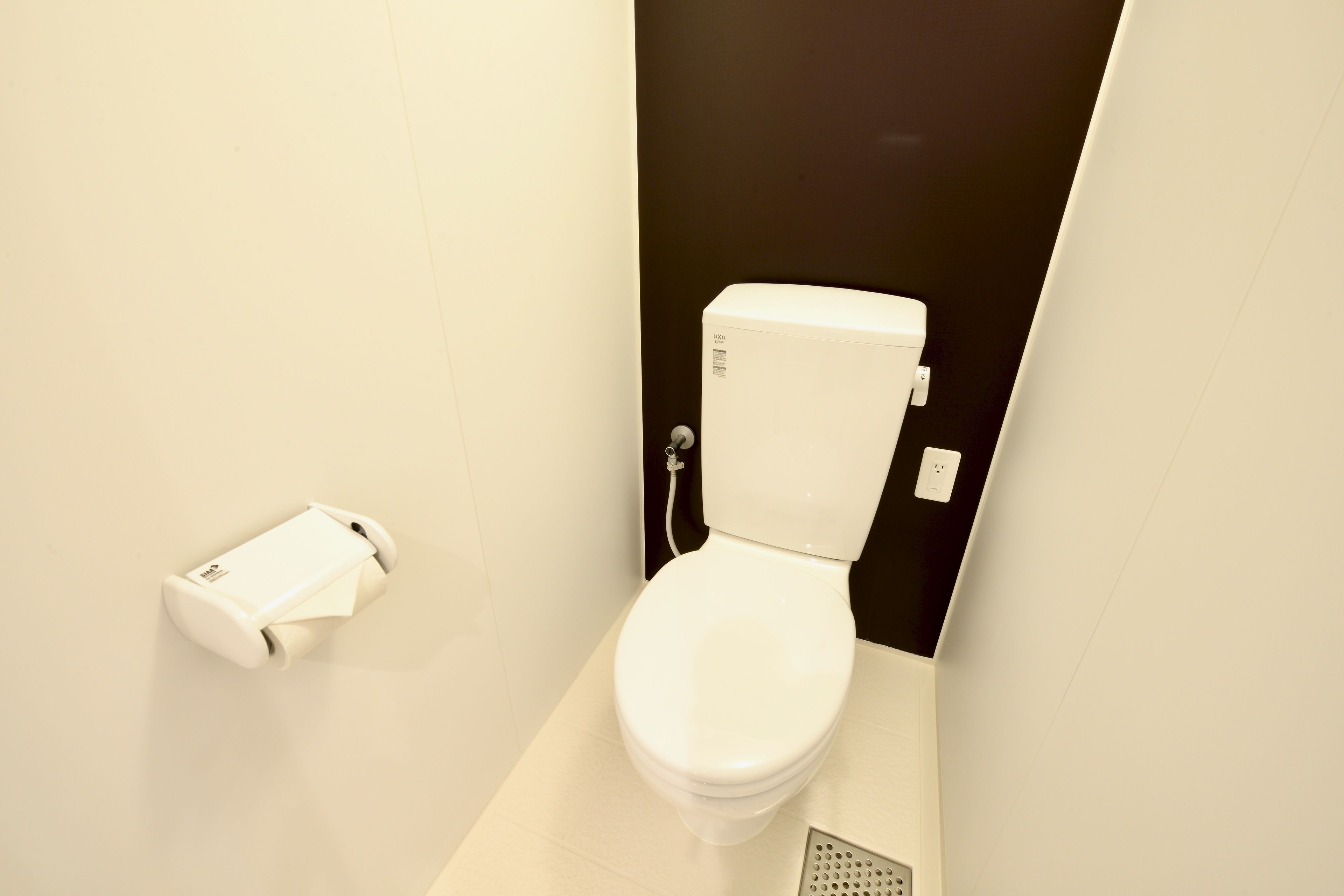 A modern bathroom with a white toilet, a toilet paper holder, and a floor drain.