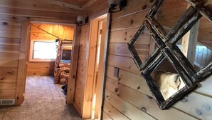 Interior de una cabaña de madera con techo inclinado, una ventana y una puerta que da a otra habitación.