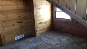Una habitación con paredes de madera, techo inclinado y una ventana pequeña.