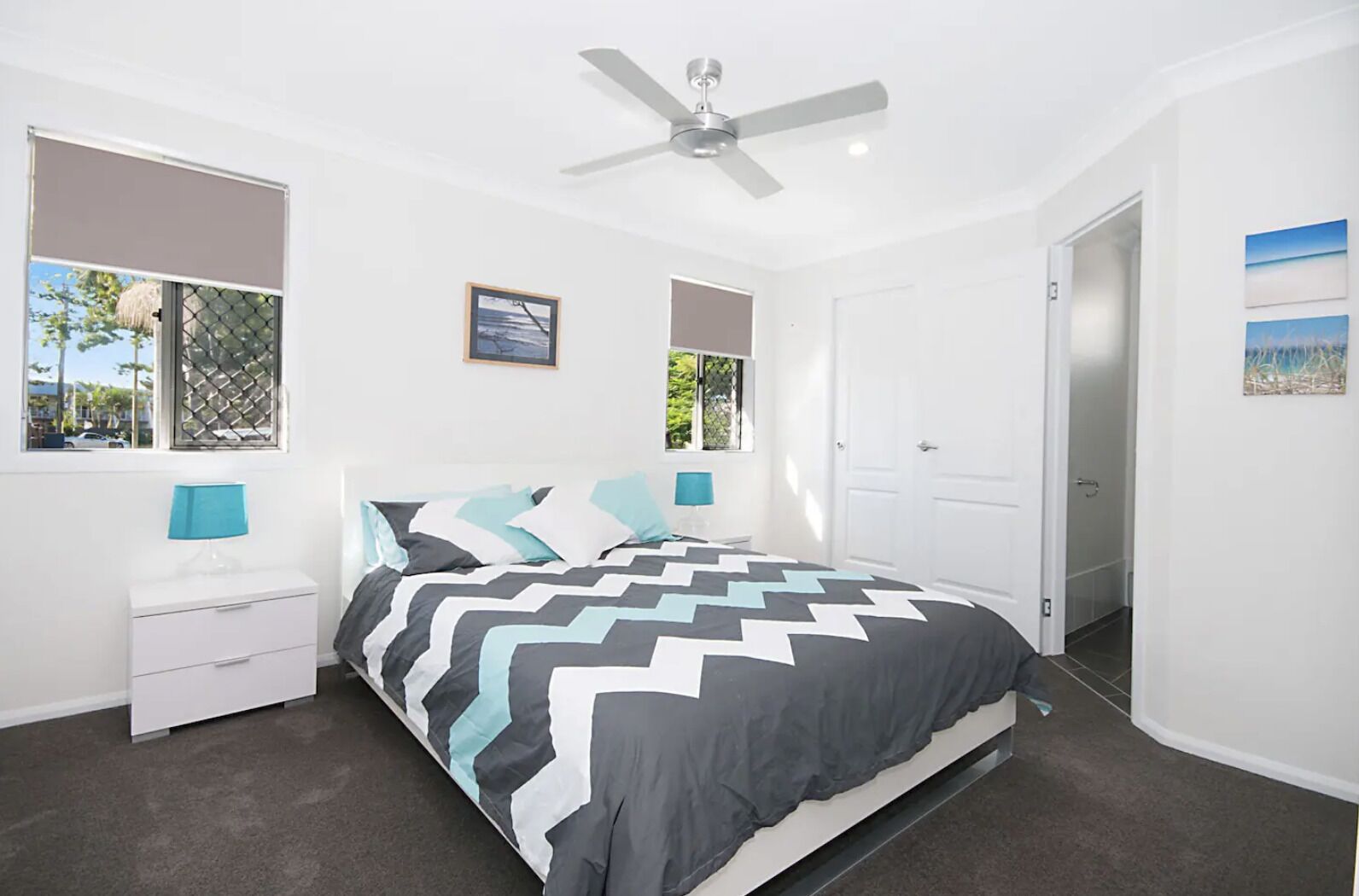A bedroom with a bed, two bedside tables, a ceiling fan, and two windows with blinds.
