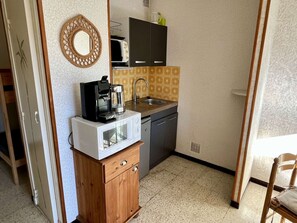 Uma cozinha compacta com cafeteira, micro-ondas e pia.