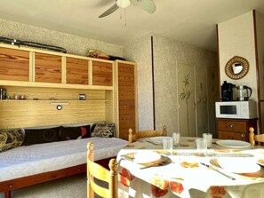 Quarto com cama, guarda-roupa de madeira, mesa de jantar com cadeiras e micro-ondas.