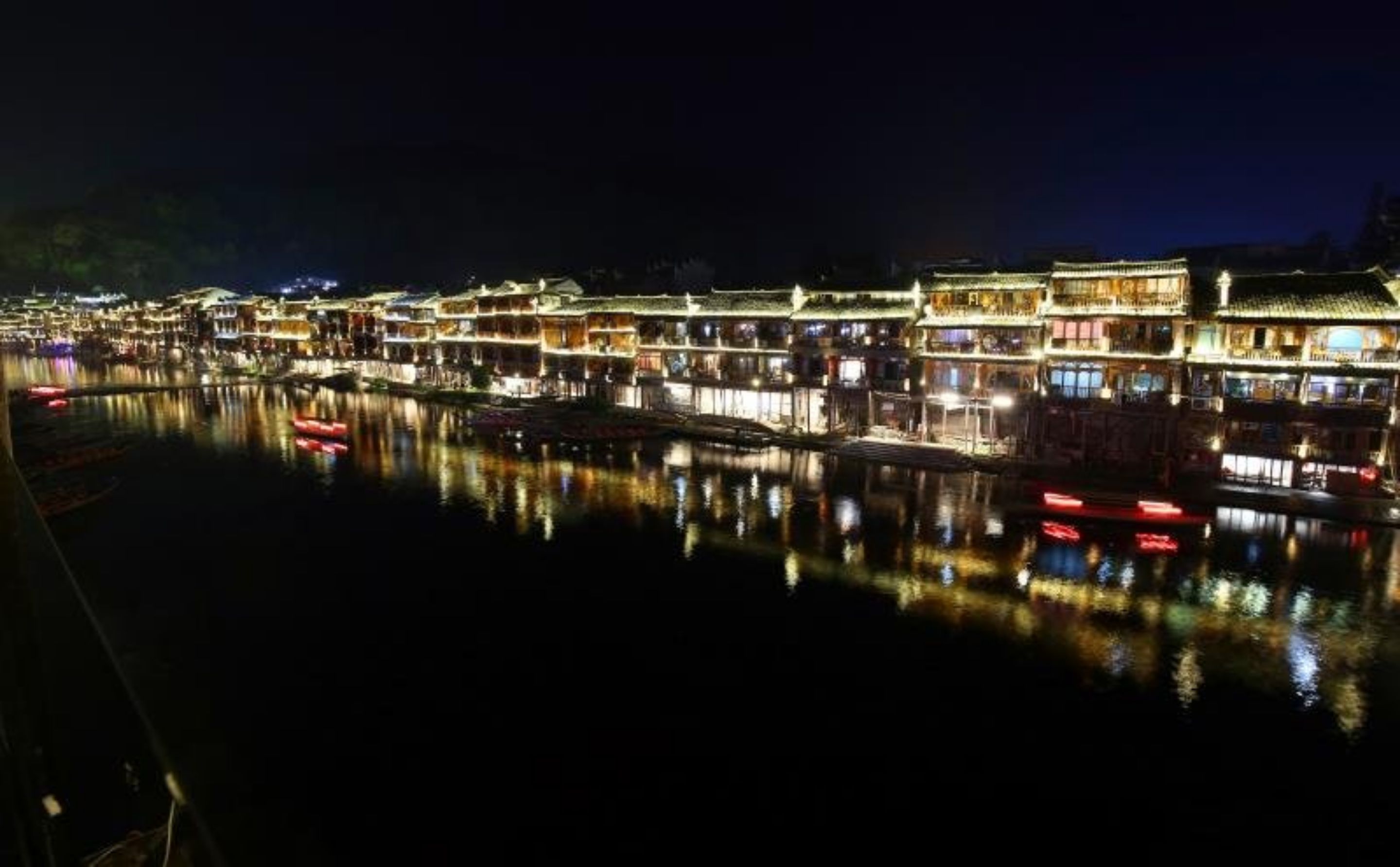 A traditional Chinese water town at night with illuminated buildings reflecting on the water.
