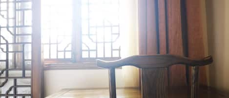 Una silla de madera tradicional con intrincados grabados, ubicada frente a una ventana con un diseño de celosía decorativa.