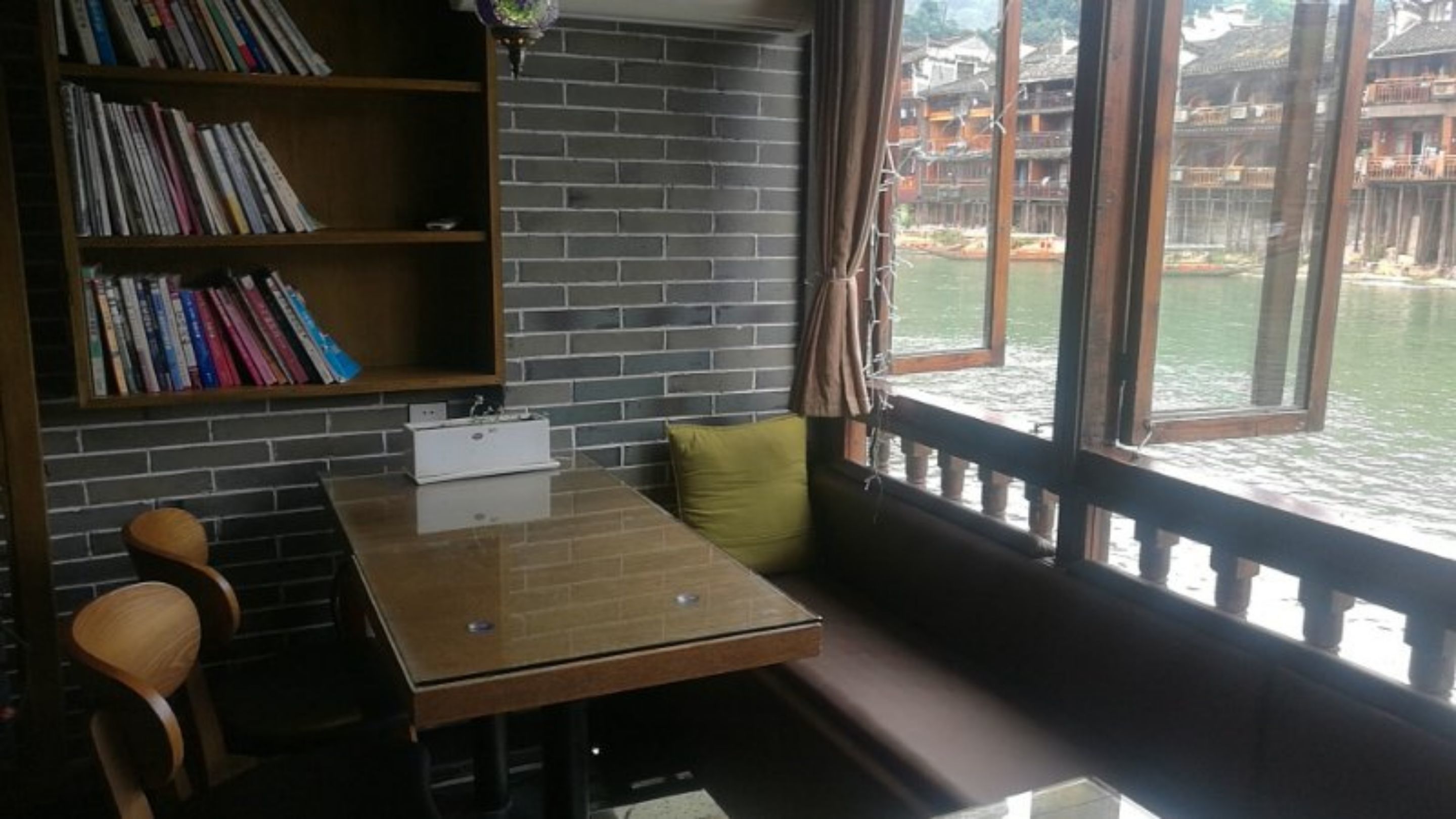 Un rincón acogedor para leer con una mesa de madera, una estantería y vistas a un edificio tradicional al otro lado del agua.