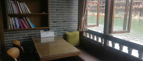 Un rincón acogedor para leer con una mesa de madera, una estantería y vistas a un edificio tradicional al otro lado del agua.