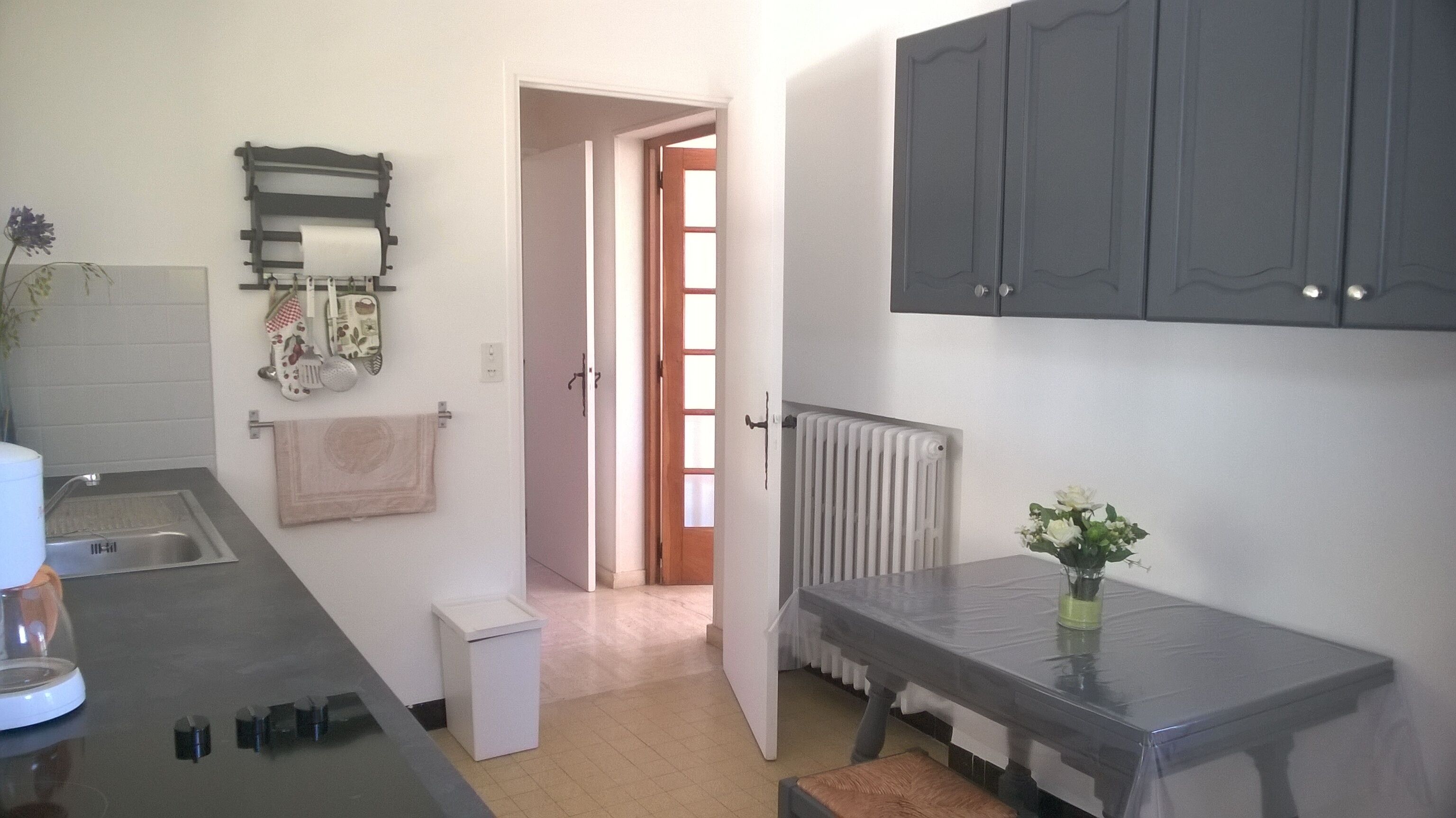 A kitchen with a sink, a small refrigerator, a white cabinet, and a table with a vase of flowers.