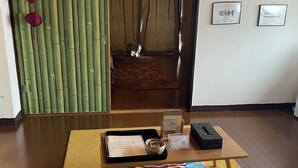 A room with a wooden floor, a tiger-themed mat, a tray with a card and a watch, and a green curtain. - 777 Takamatsu Guest House (Takamatsu)