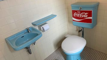 Ein Badezimmer mit blauem Waschbecken, Toilette und einem Tank mit Coca-Cola-Branding.