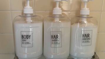 Three bottles of body soap, hair shampoo, and hair conditioner on a shelf.