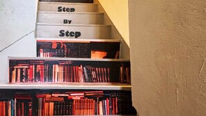 A staircase with steps labeled "Step By Step" leading to a bookshelf filled with books. - 777 Takamatsu Guest House (Takamatsu)