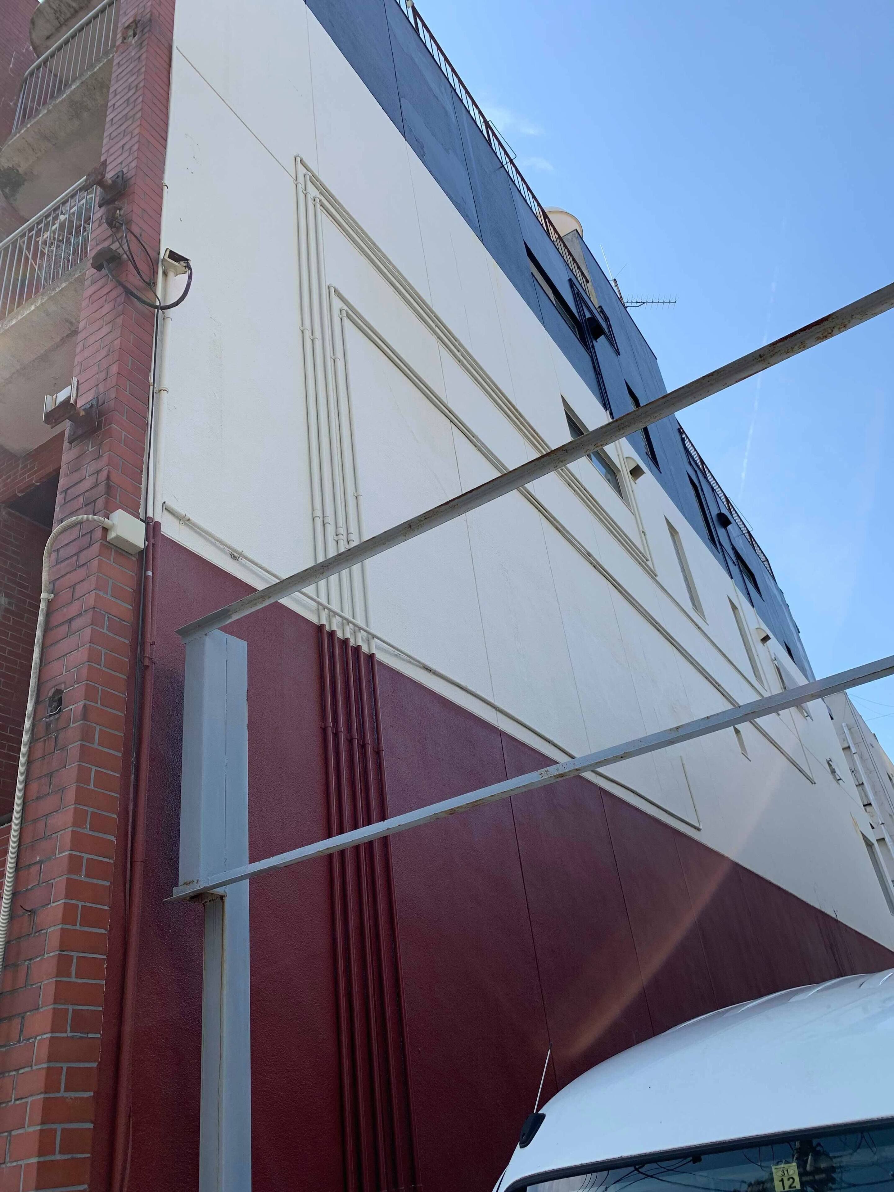 Un edificio con fachada blanca y roja, una ventana visible y una estructura metálica.