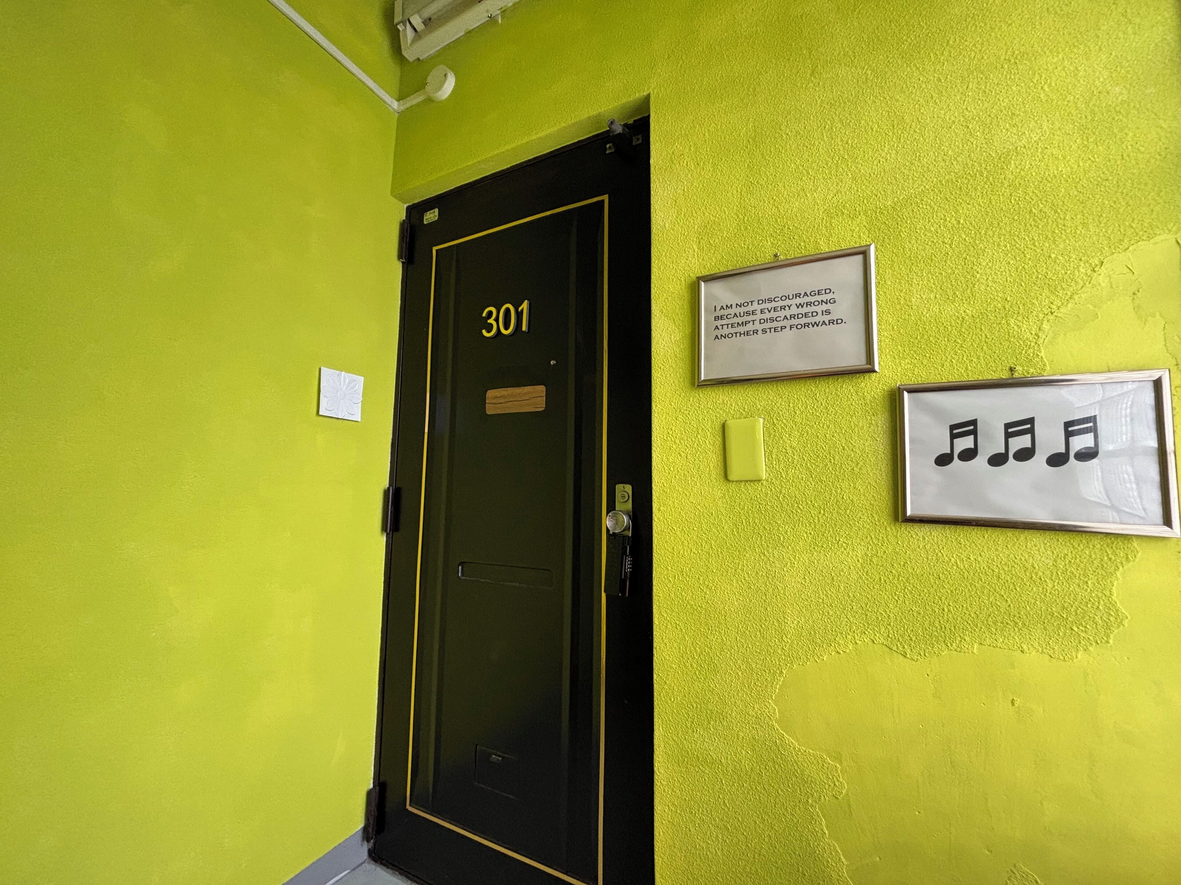 Une porte portant le numéro 301, ornée d’une citation inspirante et d’une affiche représentant une portée musicale encadrée, le tout sur un mur jaune vif.