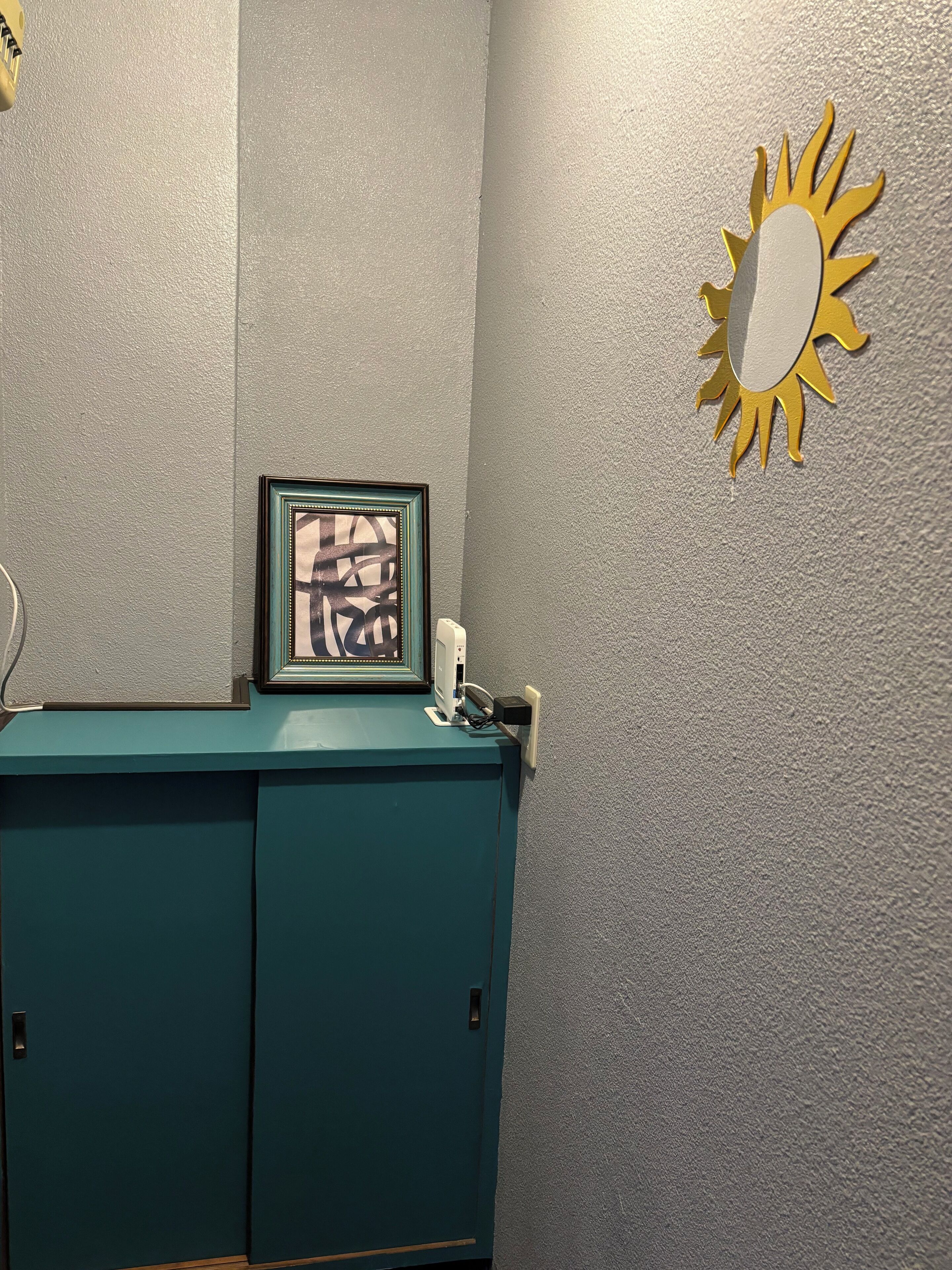 Un mueble color turquesa con un cuadro enmarco, un teléfono de pared y una decoración con forma de sol.