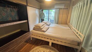 Een kamer met een bed, een houten vloer, een kamerkleed met dessin en een raam met gordijnen.
