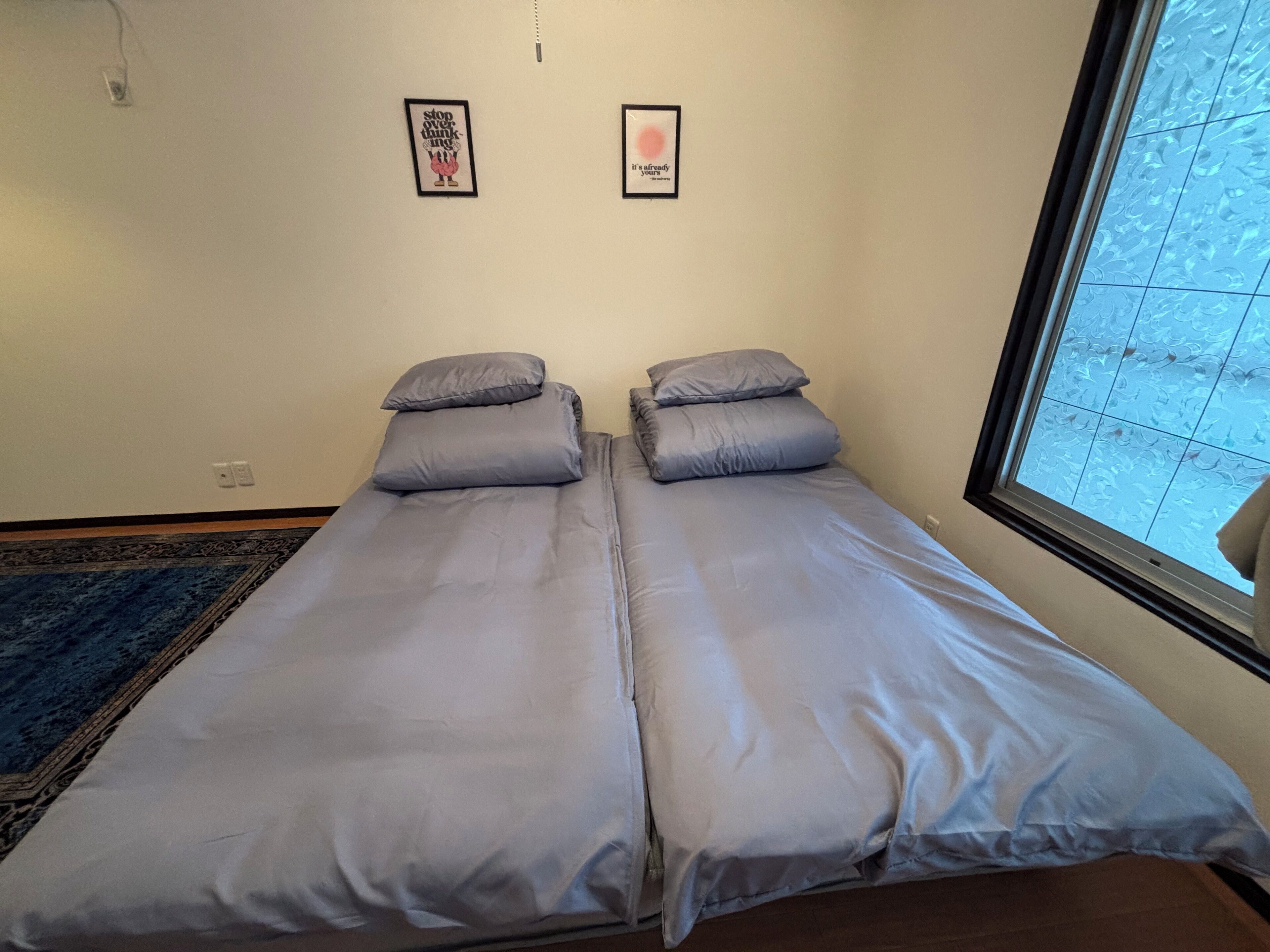 A room with two single beds, a blue rug, and two framed pictures on the wall.