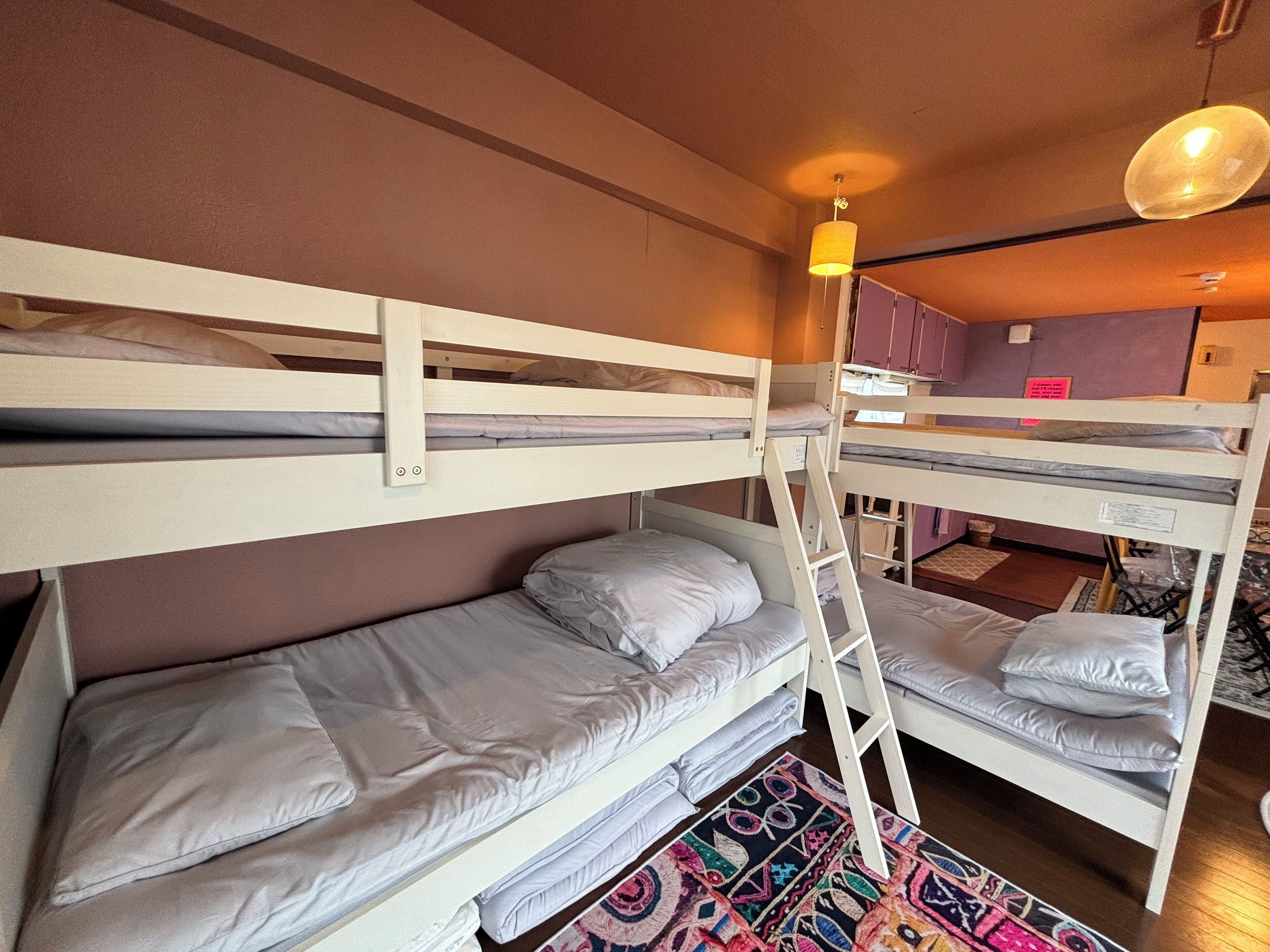 A bunk bed room with a wooden ladder, a colorful rug, and a hanging light fixture.