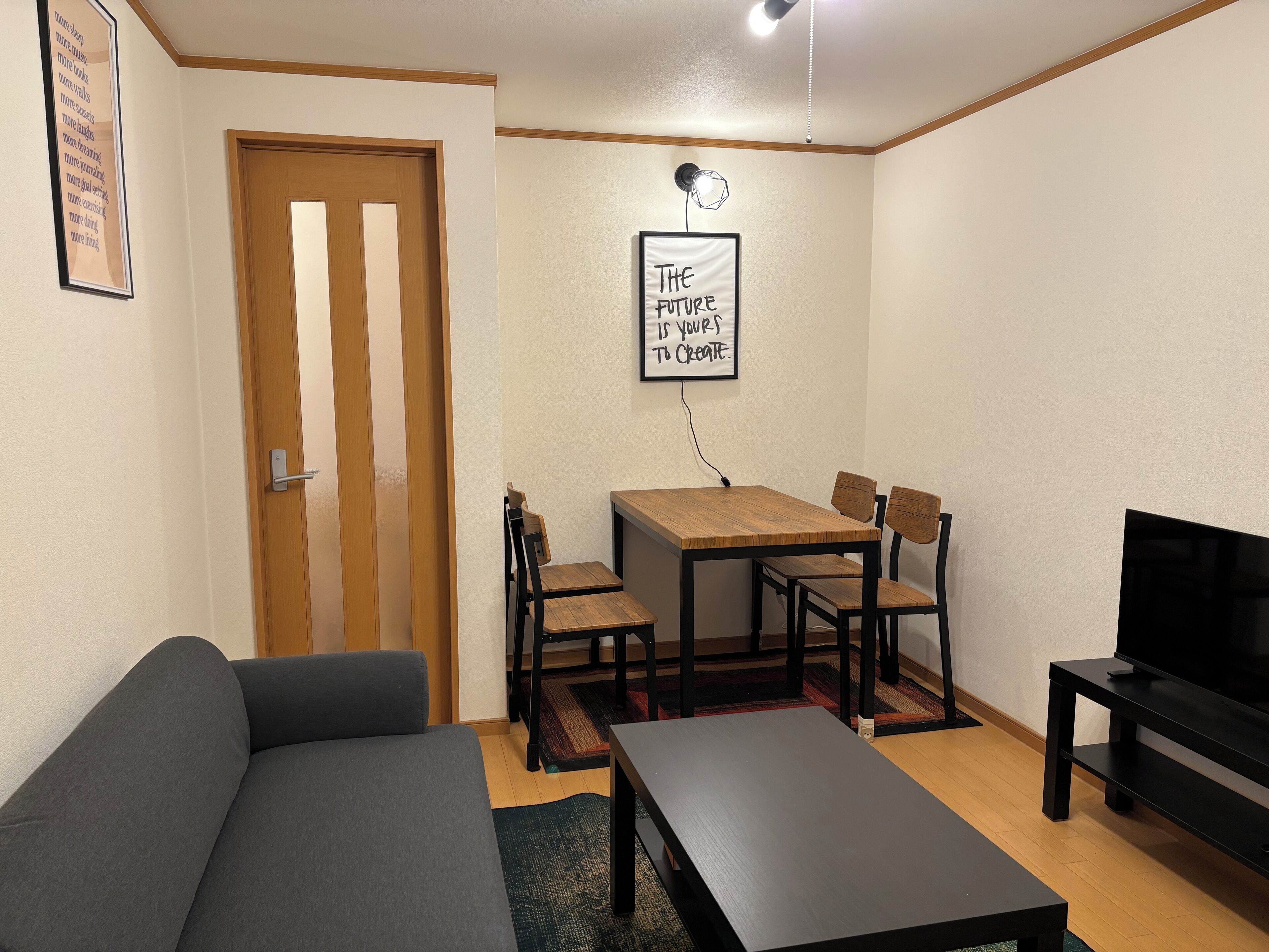 Un espacio habitable compacto con sofá, una mesa de comedor con sillas, un mueble para la televisión y un cartel motivacional en la pared.
