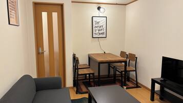 Un espacio habitable compacto con sofá, una mesa de comedor con sillas, un mueble para la televisión y un cartel motivacional en la pared.