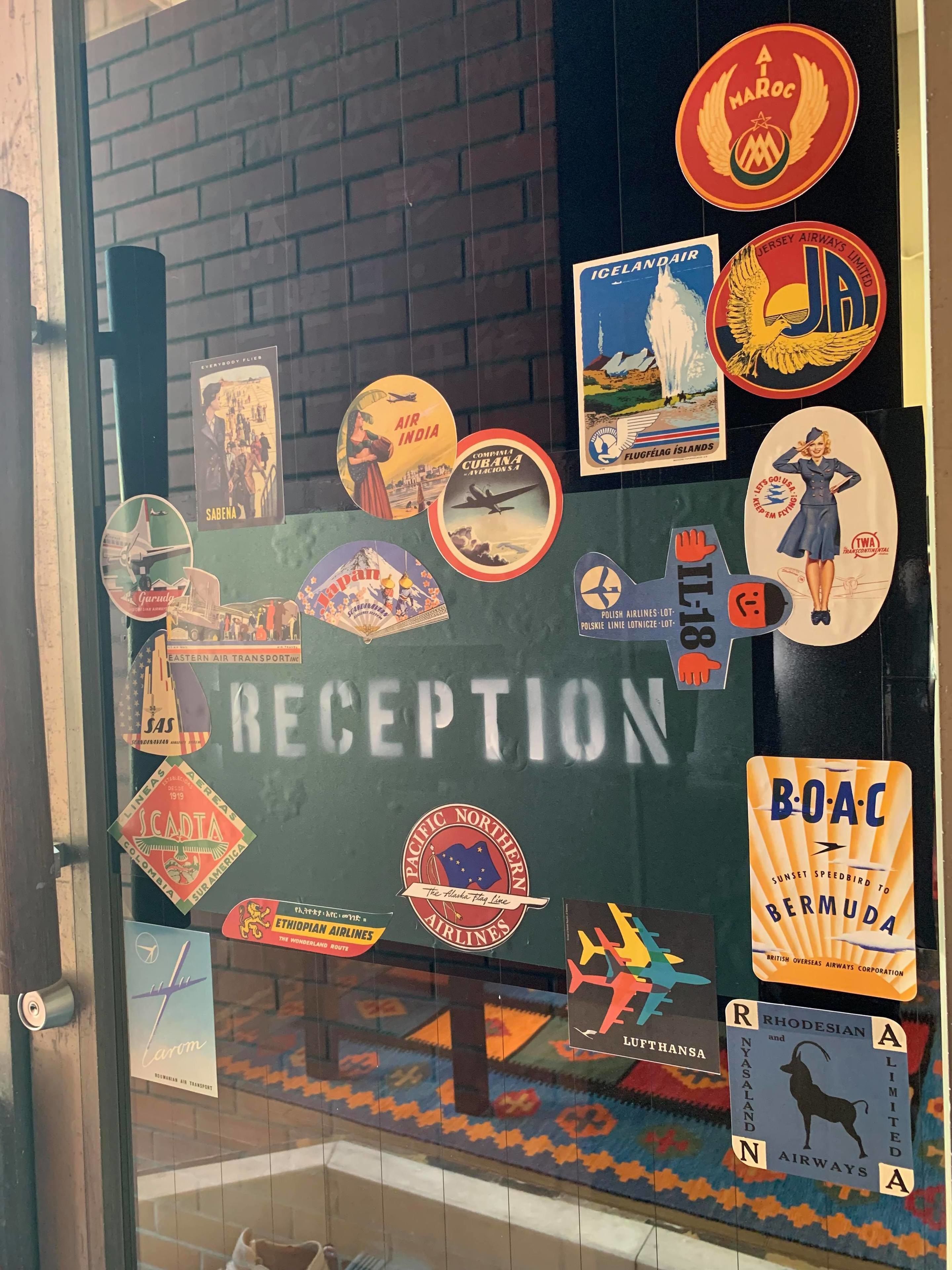 A reception area with a glass door adorned with vintage airline and travel-related stickers.