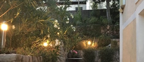 Una escalera de piedra que sube hacia un edificio, rodeada de follaje y plantas en macetas.