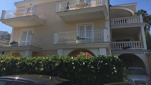 Un immeuble à plusieurs étages doté de balcons, une voiture garée devant et un arbuste au premier plan.