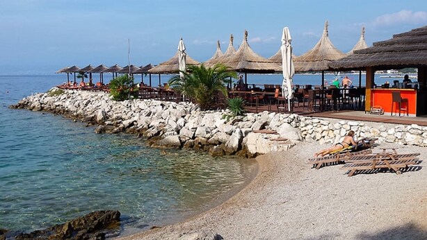 Un restaurant situé en bord de mer, doté d’une terrasse, d’une côte rocheuse et de parasols en chaume.