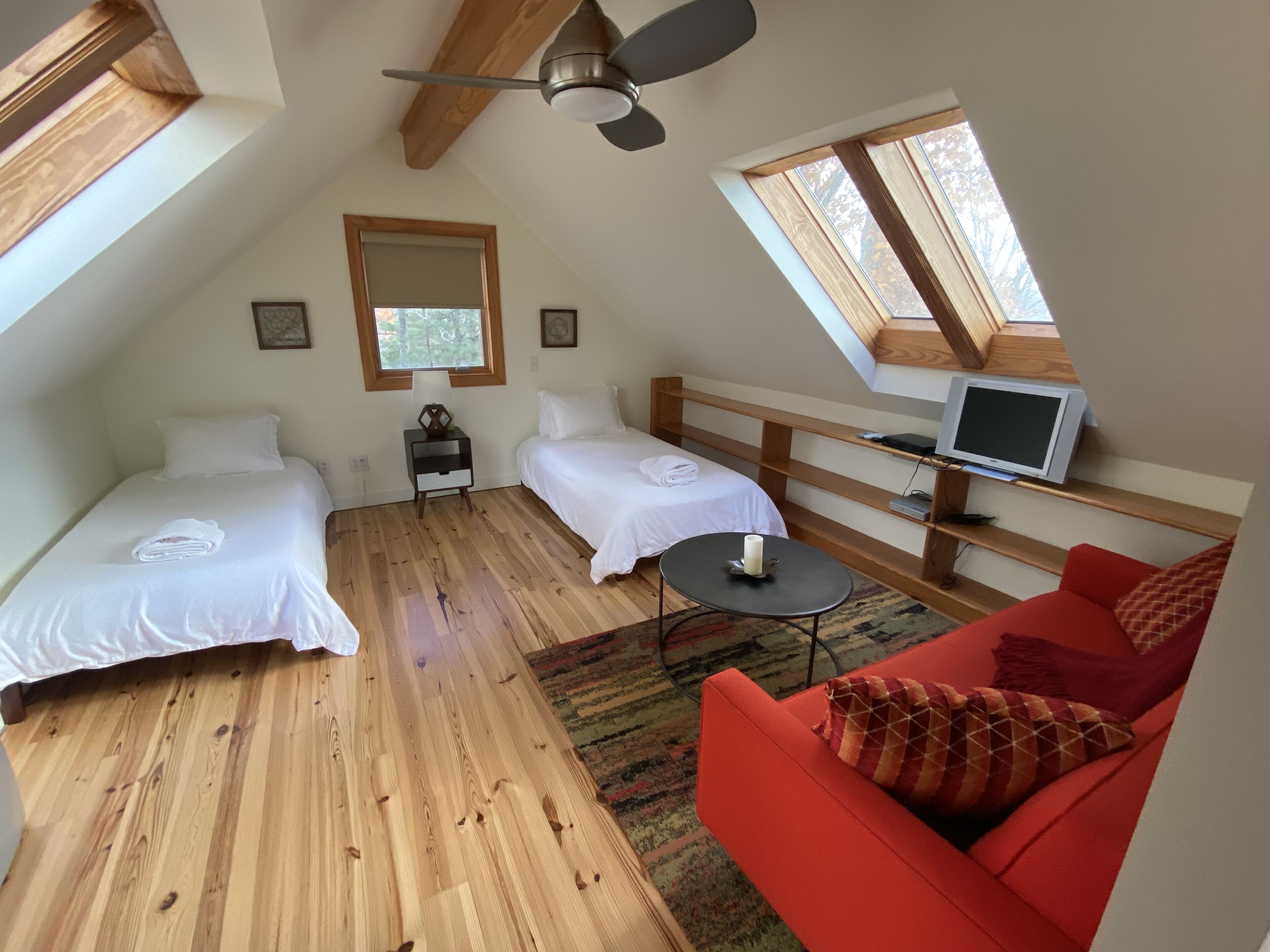 A small, cozy room with two beds, a red sofa, a TV, and a ceiling fan.