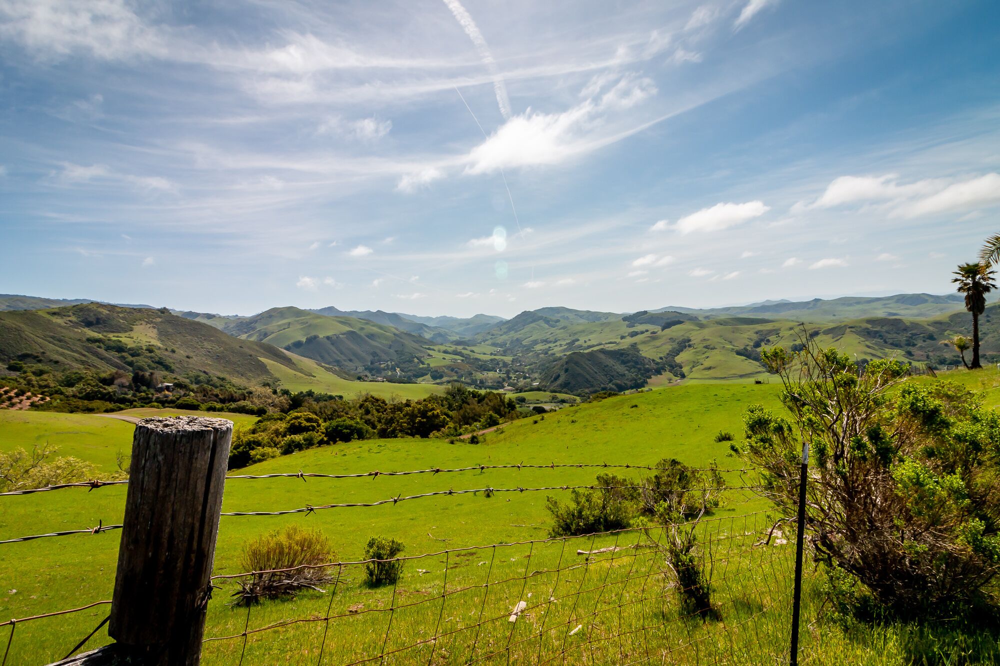 A rural landscape with rolling hills, a wooden post, and a barbed wire fence.