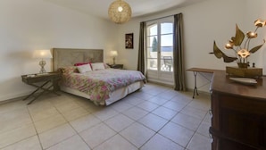Un dormitorio con cama, mesitas de noche, lámpara colgante, ventana con cortinas y vistas al exterior.