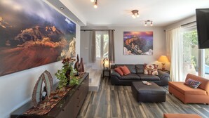 Un salon moderne avec un grand tableau, un canapé, un pouf et un téléviseur.
