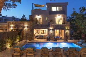 Ein modernes, zweistöckiges Haus mit Swimmingpool, Sitzgelegenheiten im Freien und einer gut beleuchteten Terrasse.