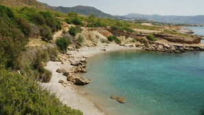 Un paysage côtier avec une plage de sable fin, une côte rocheuse et des montagnes à l’horizon.
