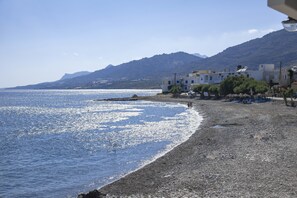 Eine Küstenlandschaft mit Kiesstrand, Gebäuden und Bergen im Hintergrund.
