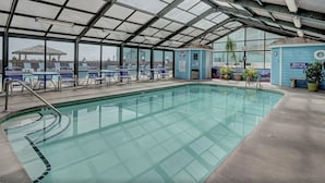 An indoor swimming pool with clear glass walls, blue lounge chairs, and a lifeguard station.