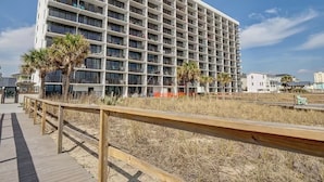 A large, multi-story hotel with a grid-like facade, located near a beach with a wooden boardwalk.