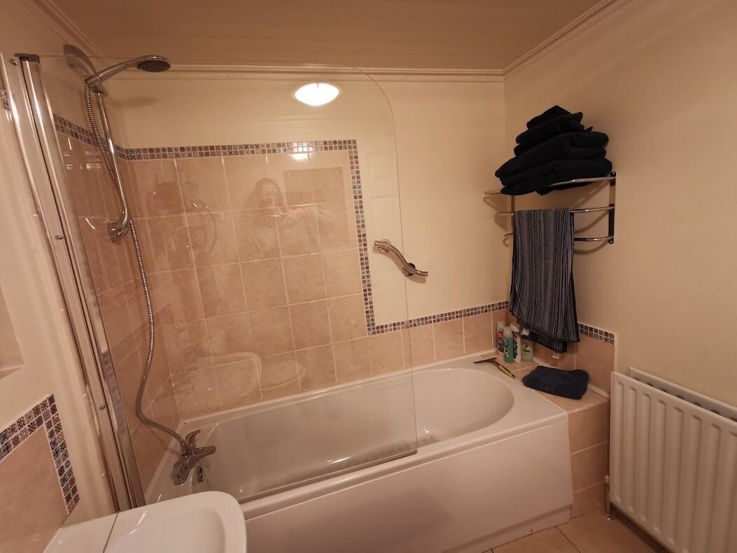Un baño con ducha envuelta en vidrio, bañera y retrete. Hay un perchero con toallas y artículos de aseo en la pared.
