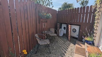 A backyard with a wooden fence, two wicker chairs, a washing machine, and potted plants.