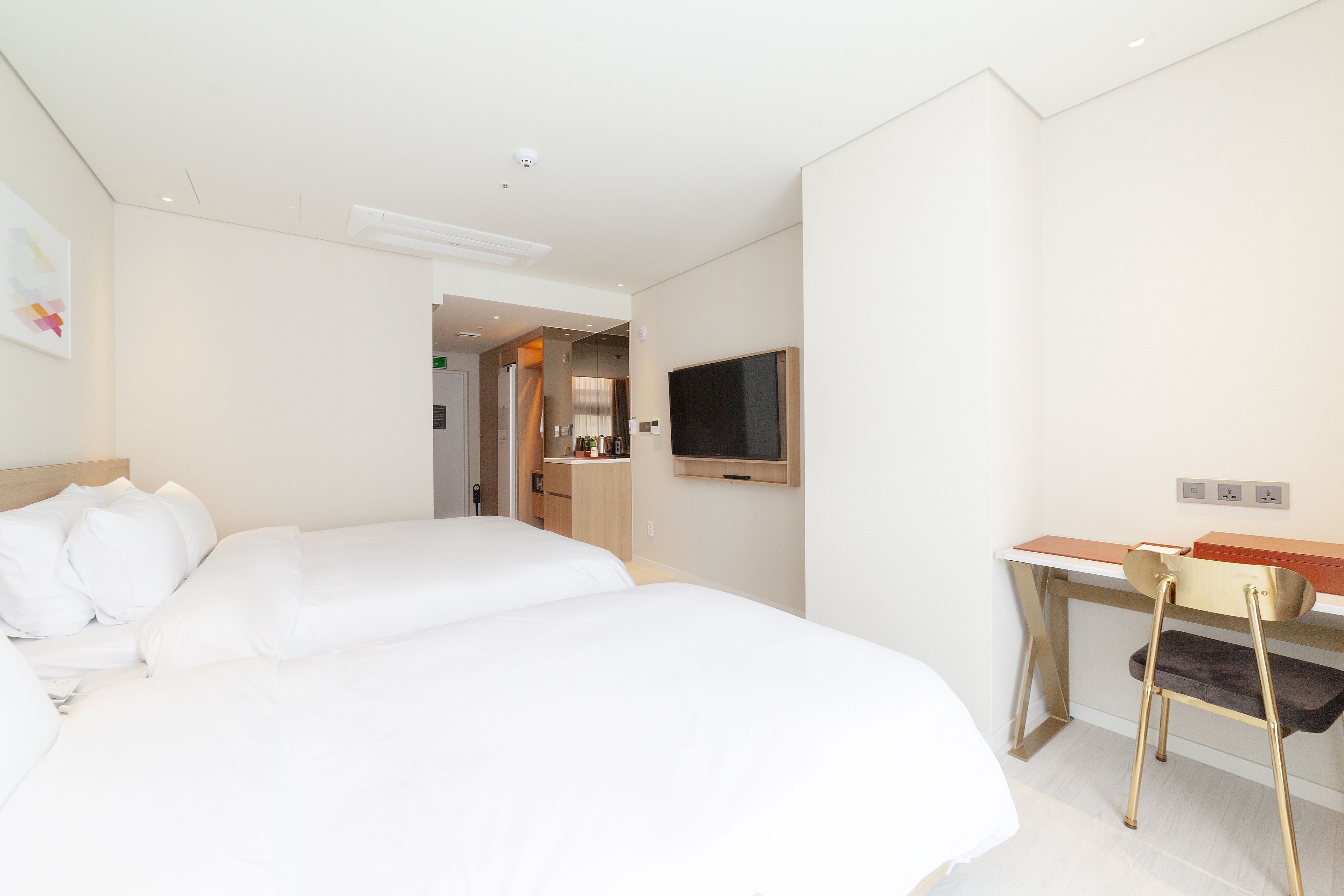 A hotel room with two beds, a desk, a chair, a television, and a kitchenette.