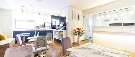 Una hall d'albergo moderna con una reception, un'area lounge e una cucina sullo sfondo.