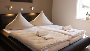 Una cama bien hecha con sábanas y almohadas blancas, un cuadro de un atardecer en la pared y una ventana con vistas al exterior.