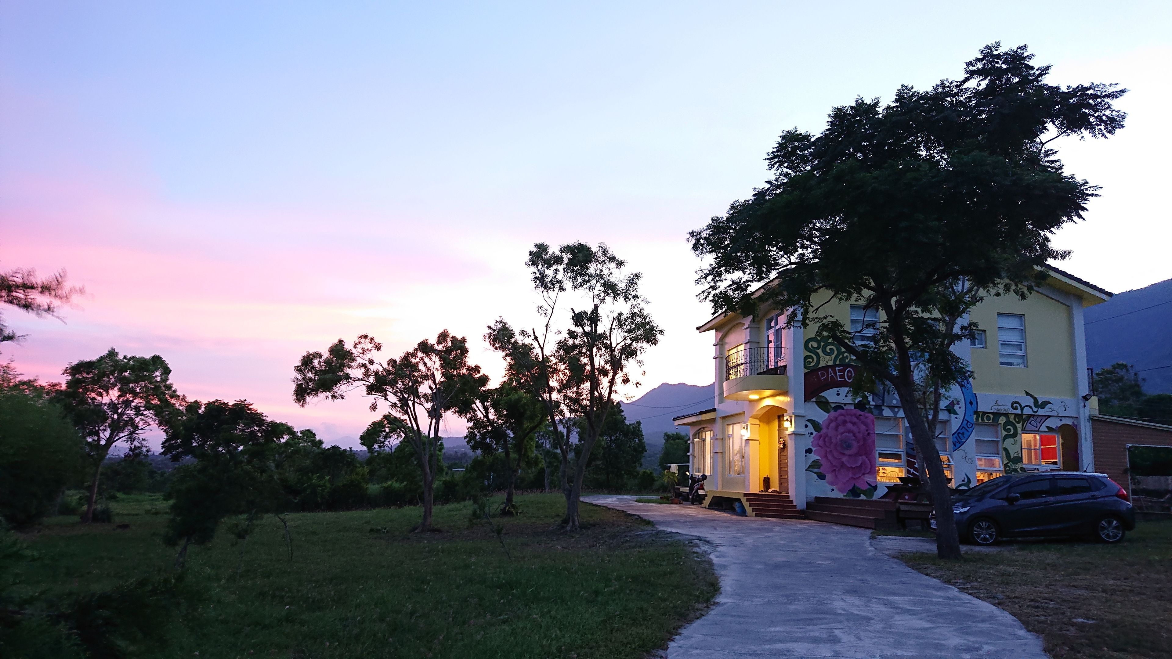 A two-story house with a paved driveway leading to the entrance, surrounded by trees and a mountain in the background.