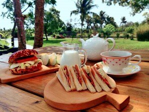 A picnic setup with sandwiches, a jug of milk, a teapot, and a cup on a wooden table in a park. - Straybirds BnB (Donghe)
